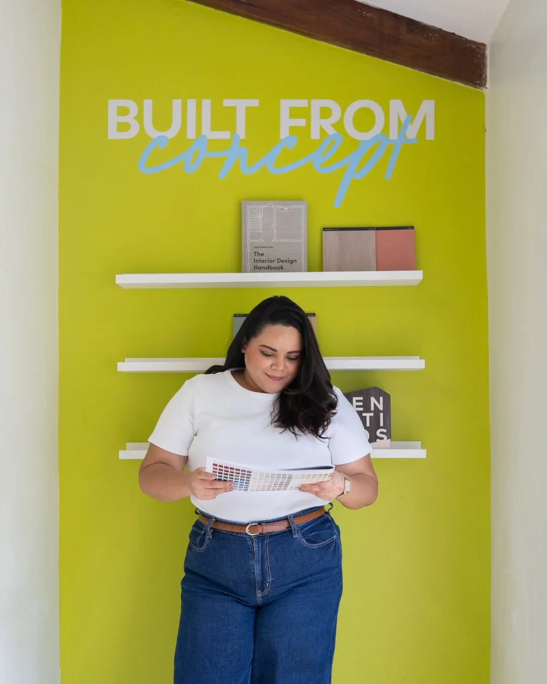 Mujer leyendo frente a una pared verde lima con repisas y el texto Built from concept.