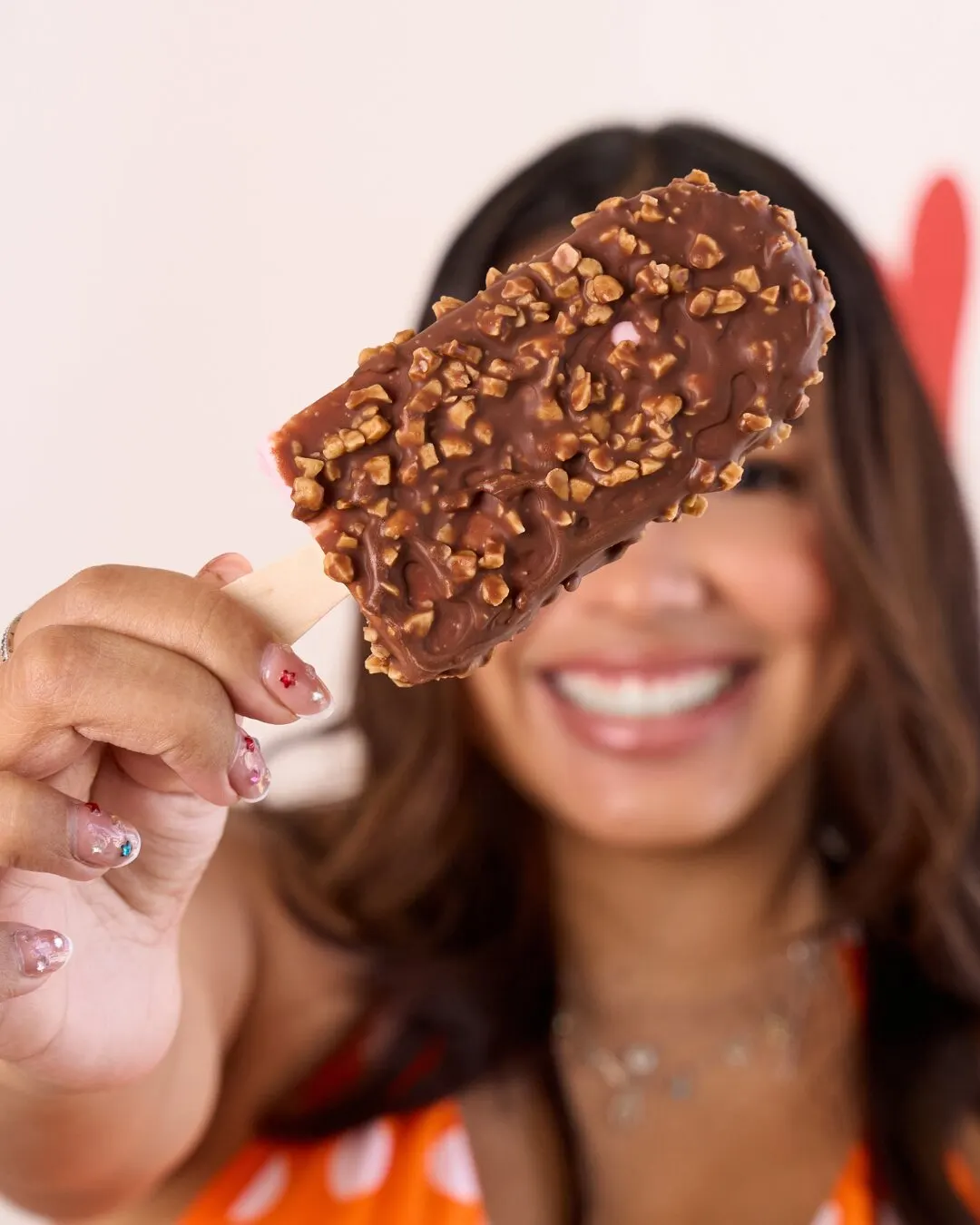 Mujer sonriente con una paleta de chocolate con trocitos frente a la cara.