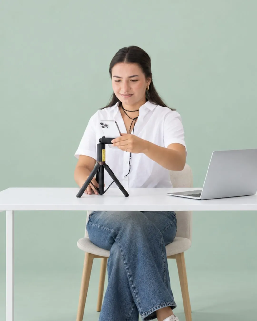 Una integrante del equipo configura un celular en un tripié sobre un fondo verde salvia